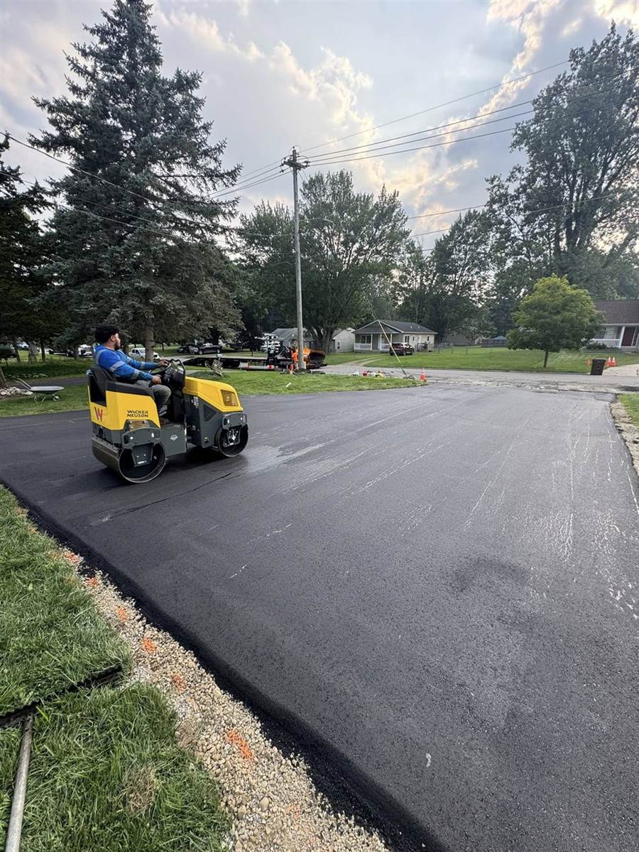 Small roller compacting a residential driveway at dusk